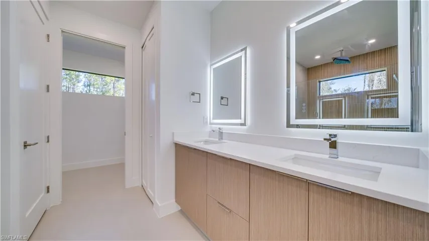 Primary bathroom with double sink vanity, custom cabinetry, backlit mirrors, quartz countertops, and private toilet.