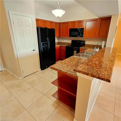 Kitchen featuring a peninsula, black appliances, pendant lighting, light tile patterned floors, and a kitchen breakfast bar