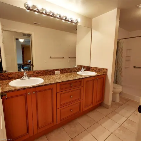 Bathroom with a shower with shower curtain, double vanity, and light tile patterned floors