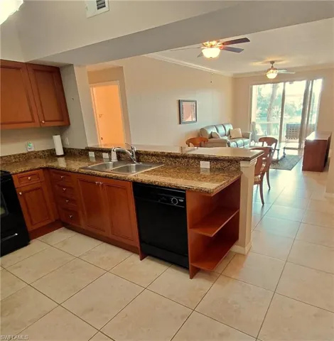Kitchen with brown cabinets, a peninsula, black appliances, open floor plan, and light tile patterned floors