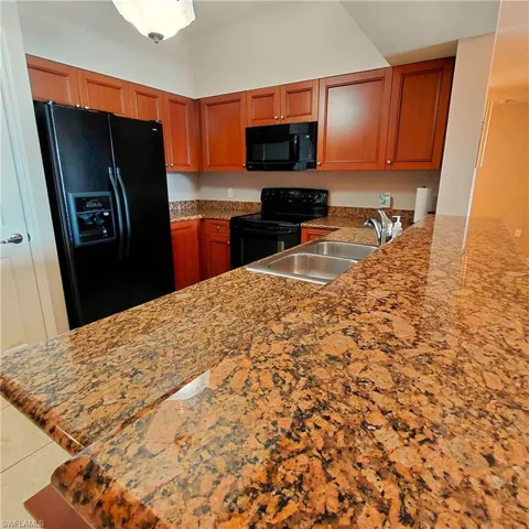 Kitchen with light stone counters, black appliances, a peninsula, brown cabinetry, and light tile patterned floors