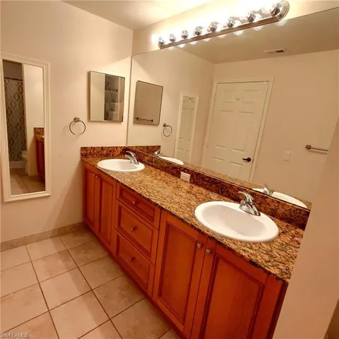 Full bathroom with double vanity, light tile patterned floors, and curtained shower