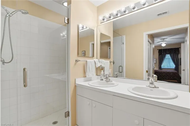 Well-appointed bathroom featuring a double vanity with two sinks, a large mirror with overhead lighting, and a glass-enclosed shower with white tiled walls