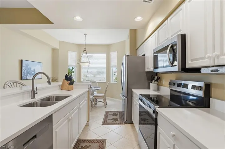 Bright kitchen featuring white cabinetry, stainless steel appliances, a double basin sink, and tiled floors
