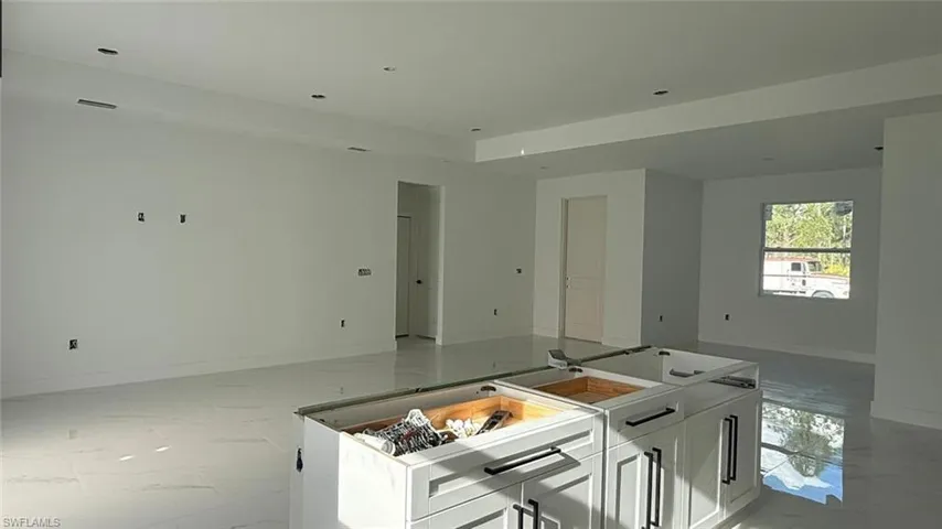 Kitchen with open floor plan, white cabinetry, baseboards, marble finish floor, and a kitchen island