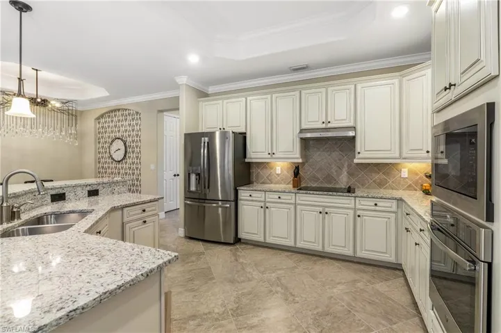 Kitchen featuring a tray ceiling, crown molding, light stone counters, stainless steel appliances, and cream cabinets