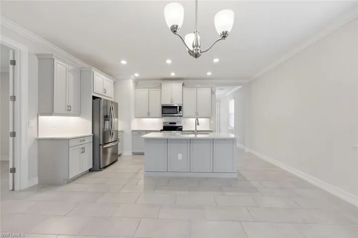 Kitchen with stainless steel appliances, ornamental molding, hanging lights, an island with sink, and decorative backsplash