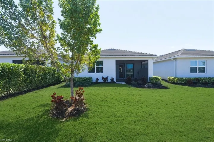 Rear view of property featuring stucco siding, a lawn, a sunroom, and a tile roof