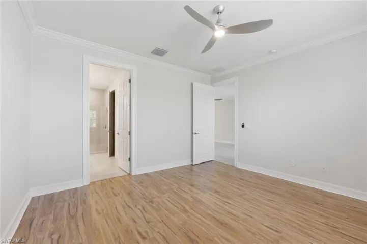 Unfurnished bedroom featuring a ceiling fan, crown molding, light wood-style flooring, and connected bathroom