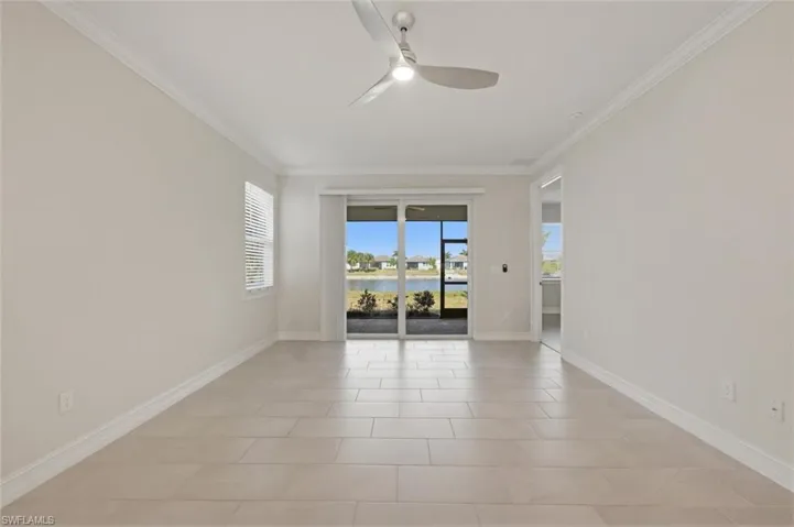 Empty room featuring a water view, a ceiling fan, healthy amount of natural light, ornamental molding, and light tile patterned floors