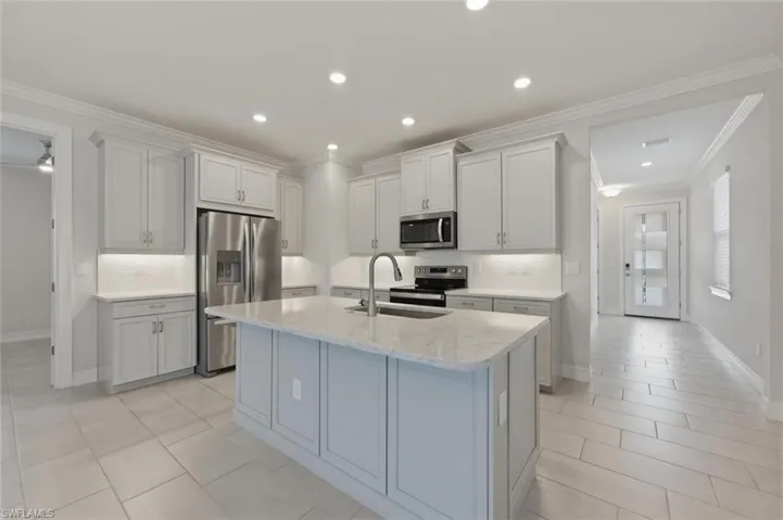 Kitchen with backsplash, ornamental molding, stainless steel appliances, light stone countertops, and recessed lighting
