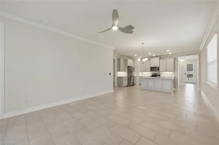 Unfurnished living room featuring suspended lighting, crown molding, and a ceiling fan
