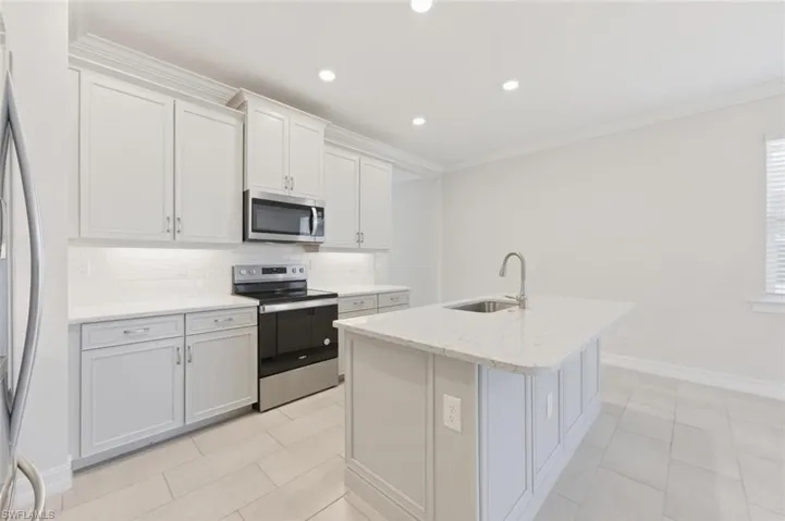 Kitchen featuring stainless steel appliances, backsplash, light stone countertops, a center island with sink, and ornamental molding