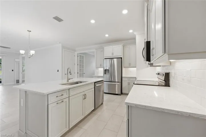 Kitchen with light stone counters, tasteful backsplash, ornamental molding, stainless steel appliances, and a center island with sink