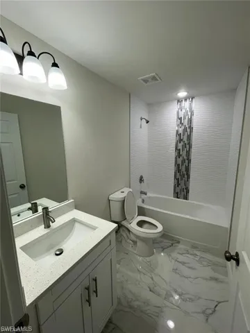 Bathroom with marble look tiles, vanity, toilet, and shower / bathtub combination