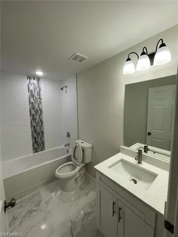 Full bathroom with vanity, toilet, shower / washtub combination, marble look tile flooring, and baseboards