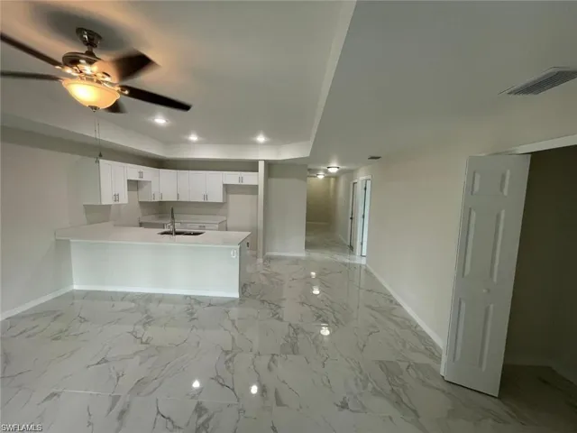 Kitchen featuring baseboards, a peninsula, a sink, a raised ceiling, and ceiling fan