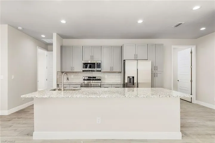 Kitchen with backsplash, an island with sink, light wood-type flooring, appliances with stainless steel finishes, and sink
