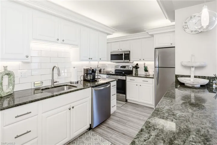 Kitchen with hanging light fixtures, a sink, dark stone counters, stainless steel appliances, and white cabinets