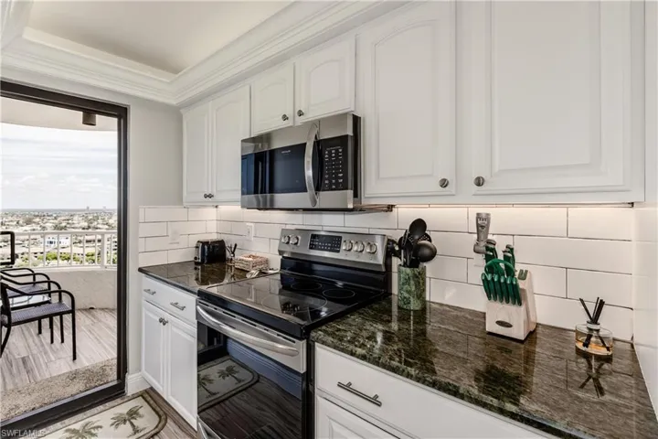 Kitchen with stainless steel appliances, dark stone countertops, ornamental molding, white cabinetry, and decorative backsplash
