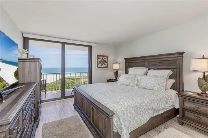 Bedroom featuring a view of the beach, a water view, access to outside, expansive windows, and light wood-type flooring