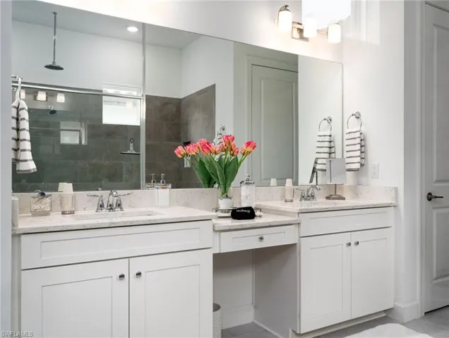 Spacious bathroom featuring a dual vanity with light-toned countertops, white cabinetry, a large wall-mounted mirror, a shower with dark gray tile surround, and a ceiling-mounted rainfall showerhead