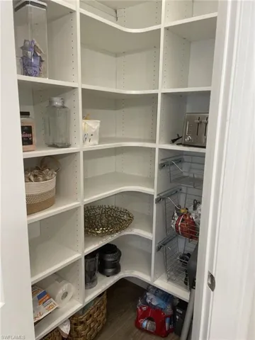 Walk-in pantry featuring white shelving, adjustable shelf heights, curved corner shelving, pull-out wire baskets, and wood-finish flooring