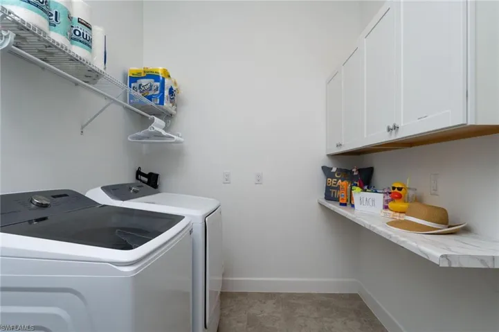 Dedicated laundry space featuring white shaker-style cabinetry, a white floating countertop, and a wall-mounted wire shelf