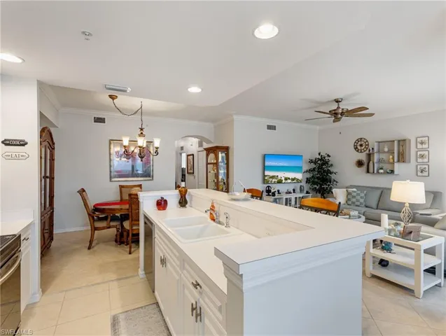 Kitchen featuring light tile patterned flooring, visible vents, arched walkways, ceiling fan with notable chandelier, and a sink