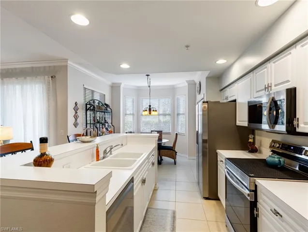 Kitchen featuring ornamental molding, appliances with stainless steel finishes, light tile patterned flooring, a sink, and a center island with sink