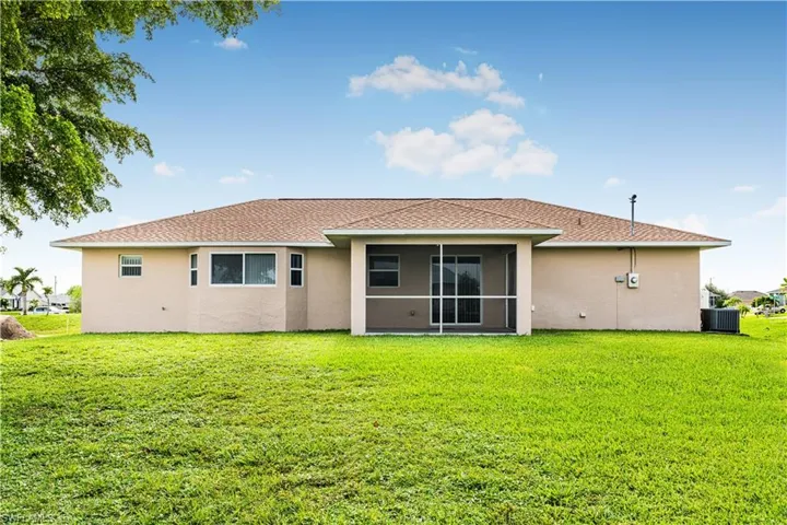 Rear view of house with a yard, central air condition unit, a sunroom, and stucco siding