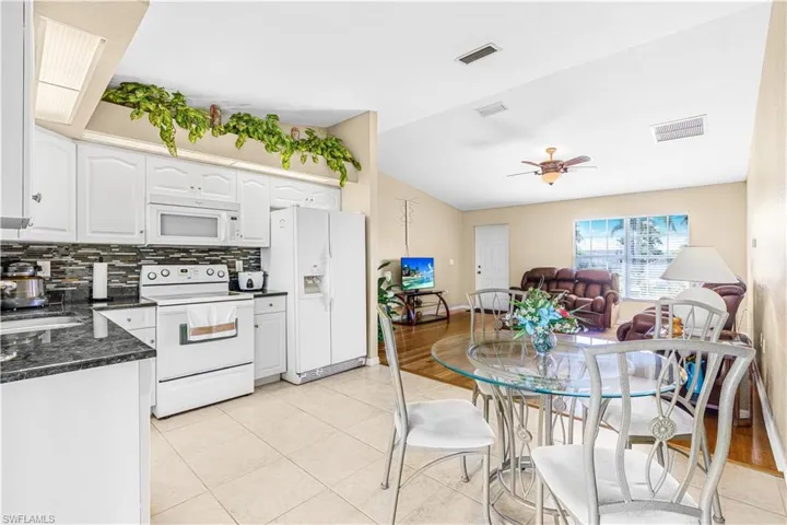 Kitchen with white appliances, backsplash, light tile patterned flooring, white cabinets, and visible vents
