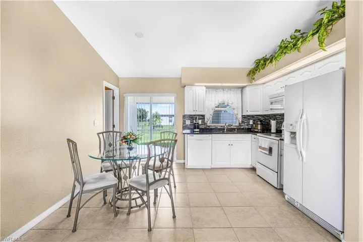 Kitchen featuring tasteful backsplash, light tile patterned floors, white cabinets, dark countertops, and white appliances