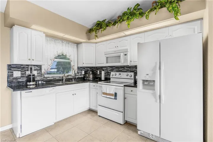 Kitchen with white appliances, backsplash, and light tile patterned floors