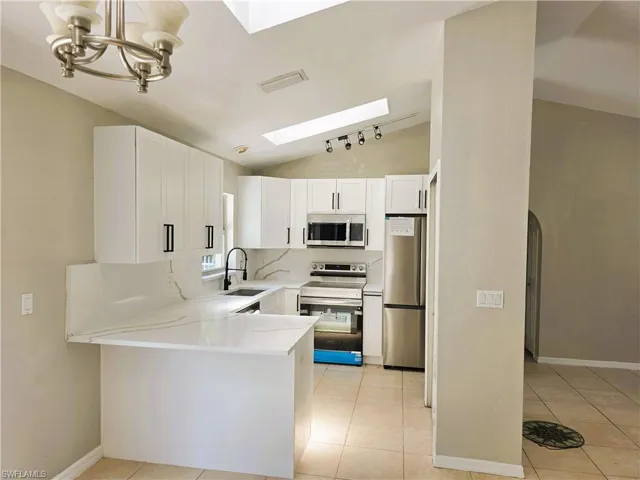 Kitchen featuring appliances with stainless steel finishes, a skylight, lofted ceiling, a peninsula, and light countertops