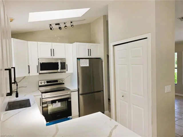 Kitchen with stainless steel appliances, vaulted ceiling, a skylight, and light stone counters