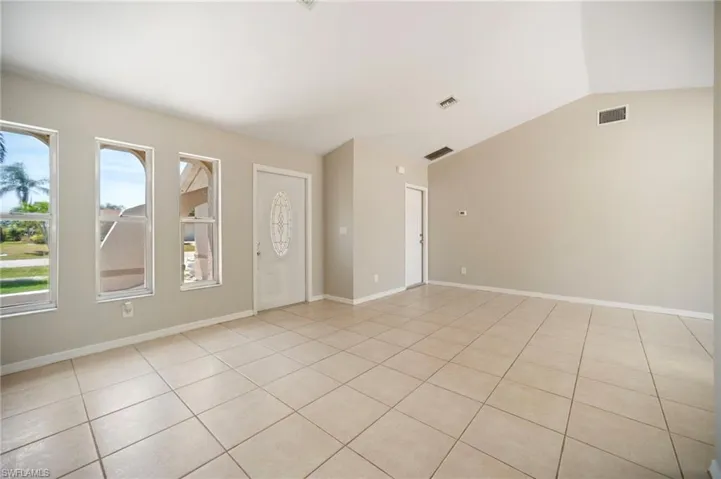 Great room with lofted ceiling, light tile patterned flooring, baseboards, and visible vents