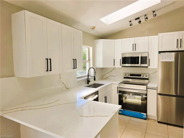 Kitchen featuring stainless steel appliances, a skylight, light stone counters, a peninsula, and vaulted ceiling