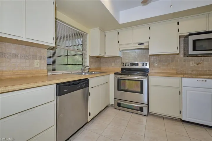 Kitchen featuring light tile flooring, backsplash, white cabinetry, appliances with stainless steel finishes, and sink