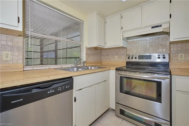 Kitchen with wall chimney exhaust hood, stainless steel appliances, white cabinets, and tasteful backsplash