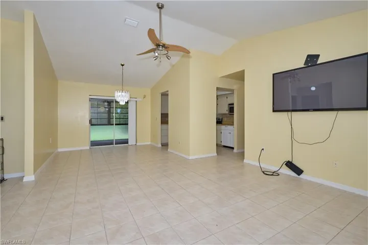 Unfurnished living room with vaulted ceiling, light tile floors, and ceiling fan with notable chandelier