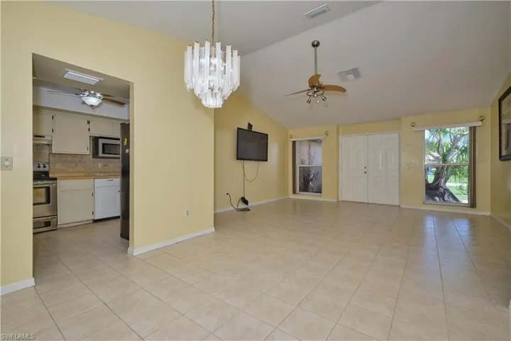 Unfurnished living room featuring ceiling fan with notable chandelier, lofted ceiling, and light tile floors