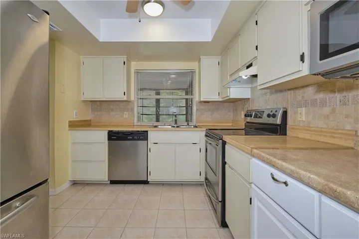 Kitchen with ceiling fan, stainless steel appliances, a tray ceiling, and white cabinetry