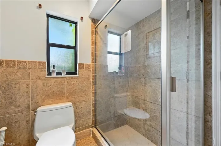 Bathroom featuring tile walls, a stall shower, and wainscoting