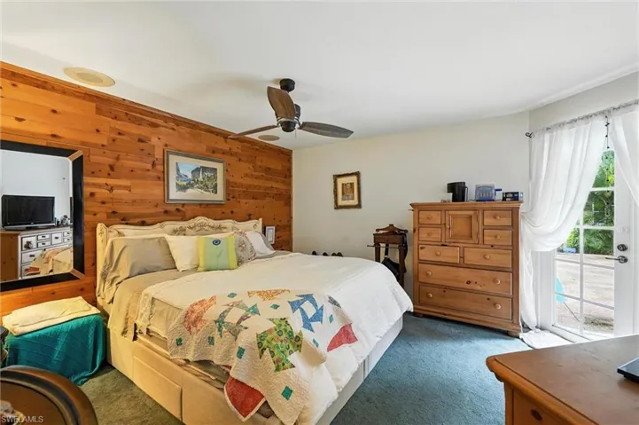 Bedroom featuring access to outside, carpet flooring, wooden walls, and ceiling fan