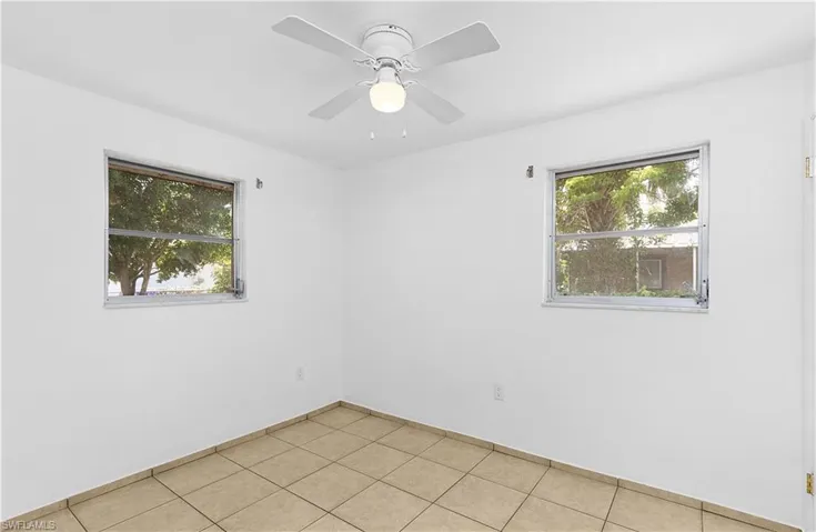 Empty room featuring ceiling fan, light tile patterned floors, baseboards, and a healthy amount of sunlight