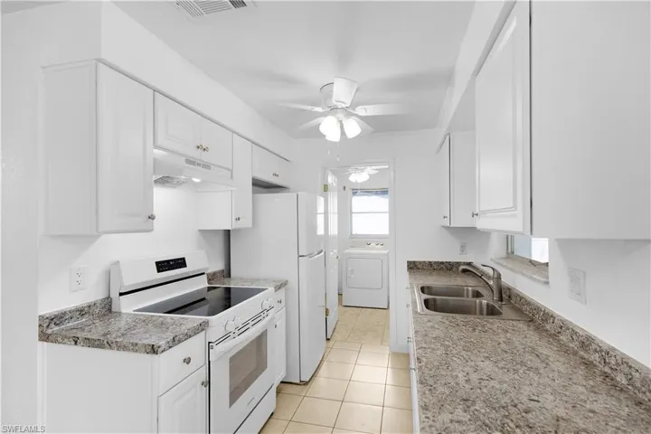 Kitchen with washer / clothes dryer, under cabinet range hood, white appliances, visible vents, and a sink