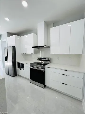 Kitchen featuring white cabinets, appliances with stainless steel finishes, backsplash, and wall chimney range hood