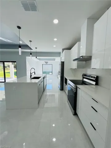 Kitchen featuring white cabinetry, sink, wall chimney range hood, decorative light fixtures, and appliances with stainless steel finishes