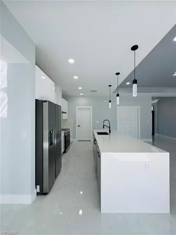 Kitchen with pendant lighting, a kitchen island with sink, white cabinets, sink, and stainless steel fridge with ice dispenser